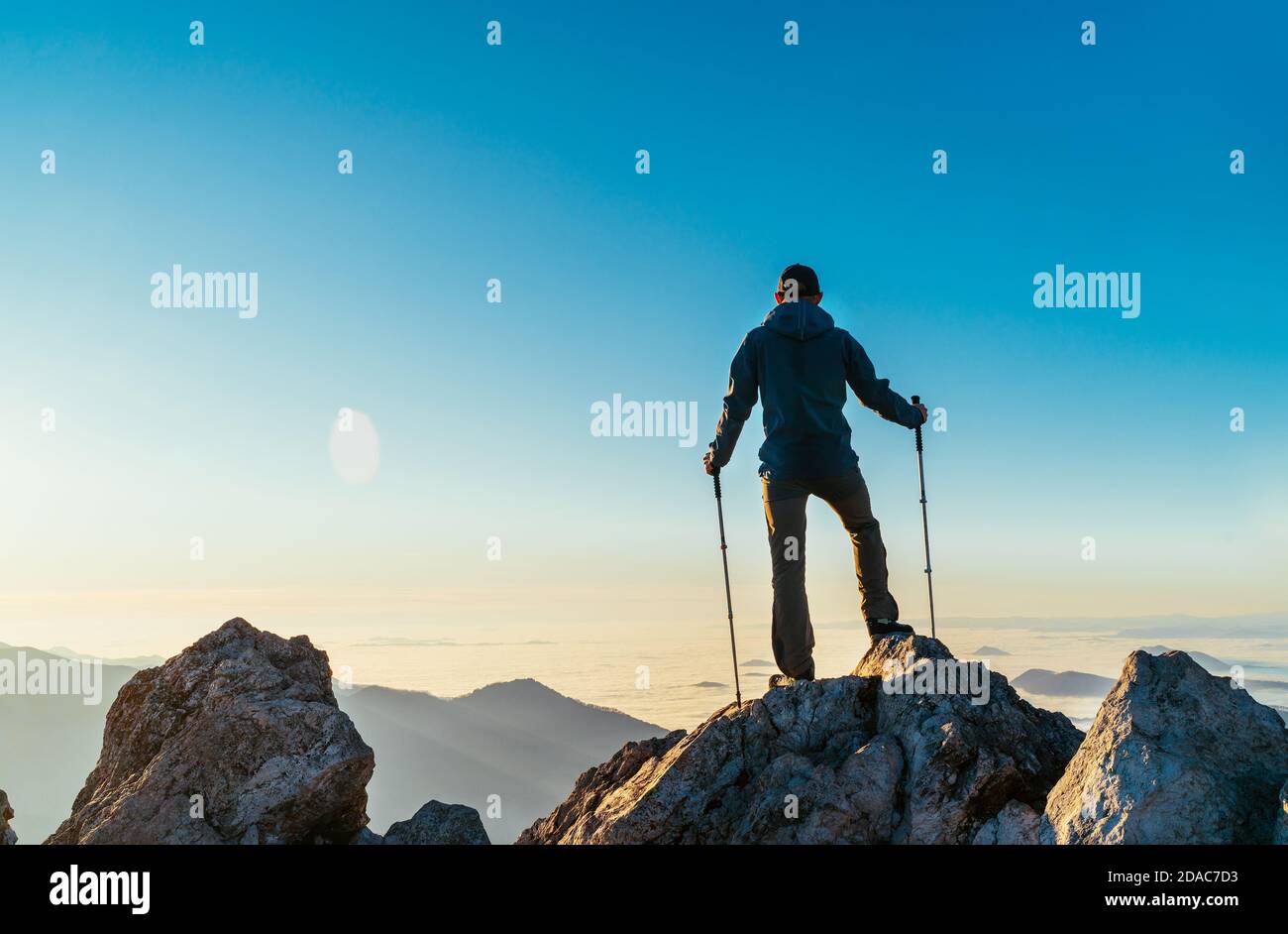 Young hiker Man standing with trekking poles on a cliff edge and looking at Tatra mountains valley covered with clouds. Successful Velky Rozsutec 1610 Stock Photo
