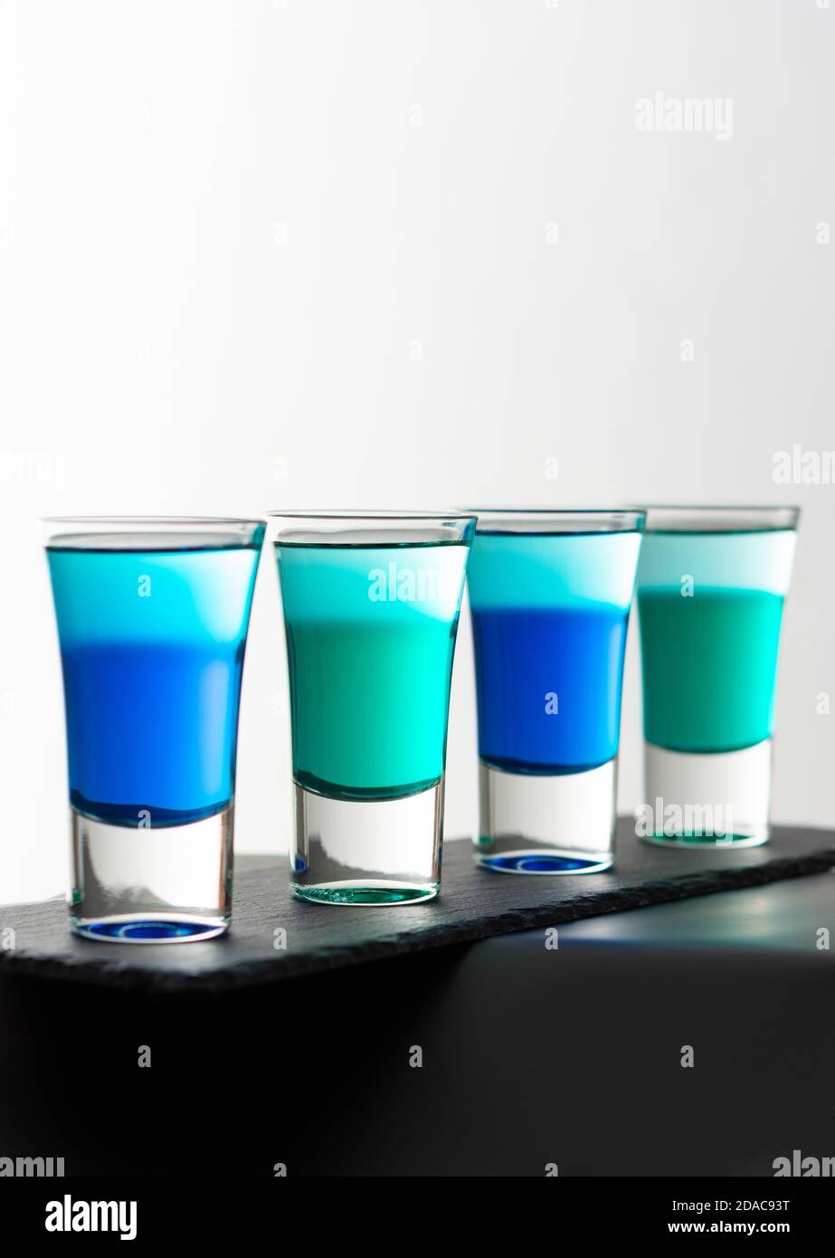Blue and green alcoholic shots, shot glasses with colored liquor on a black board close up Stock Photo