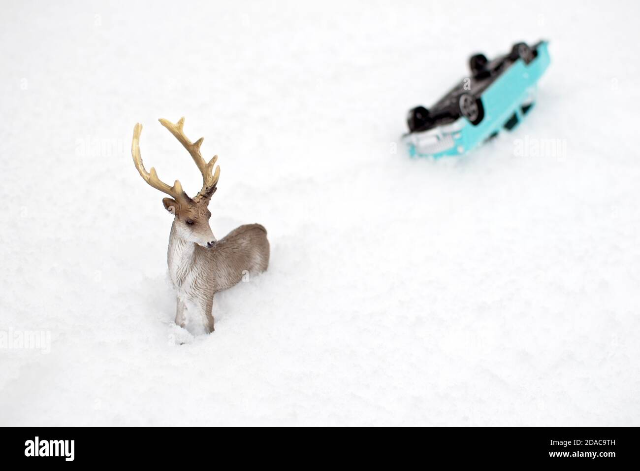 Toy deer (in focus) and inverted model of car (defocused) on the snow Stock Photo