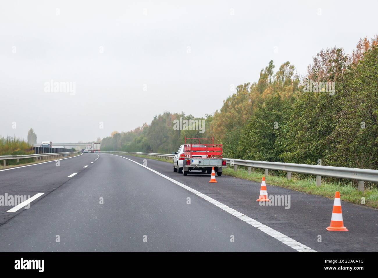 Faulty car with red trailer and traffic cones on emergency stopping lane on roadside. Problem with vehicle on the highway Stock Photo