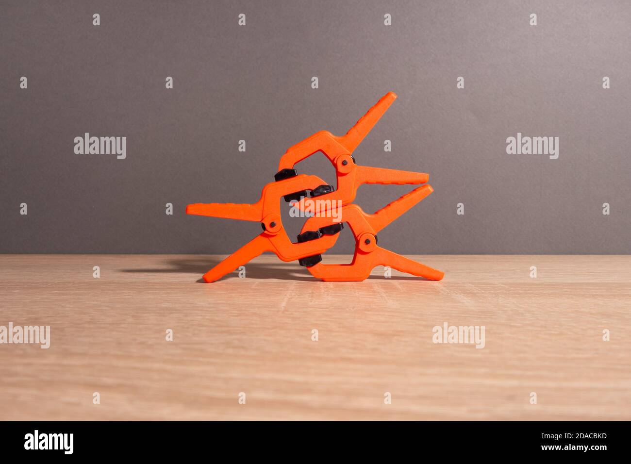 Clothespins, carpentry clamps of orange color lie on a wooden table. A pyramid in the form of a robot made of clamps. Stock Photo