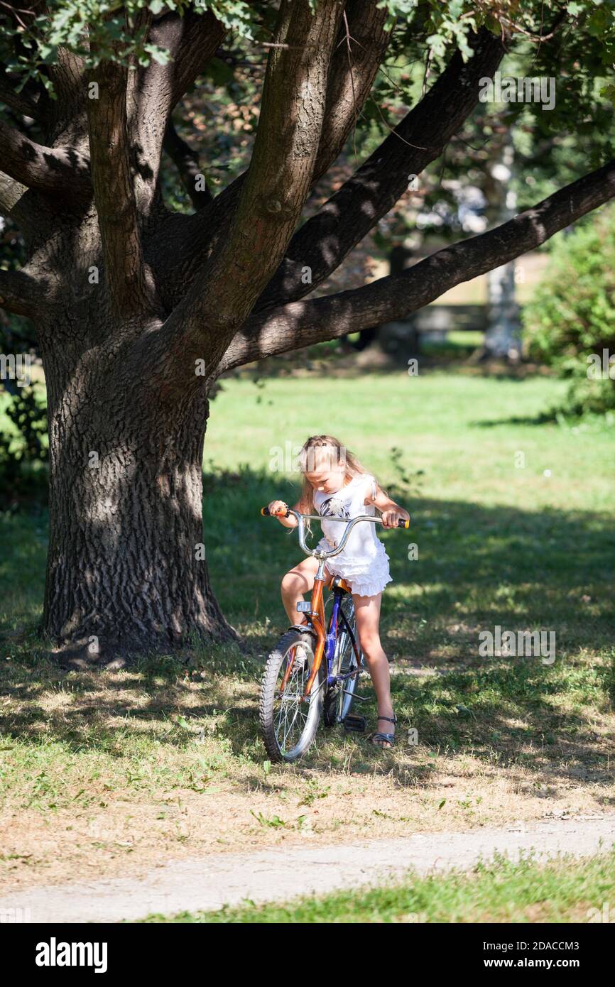 Caucasian girl learning to ride a bike in the summer park Stock Photo