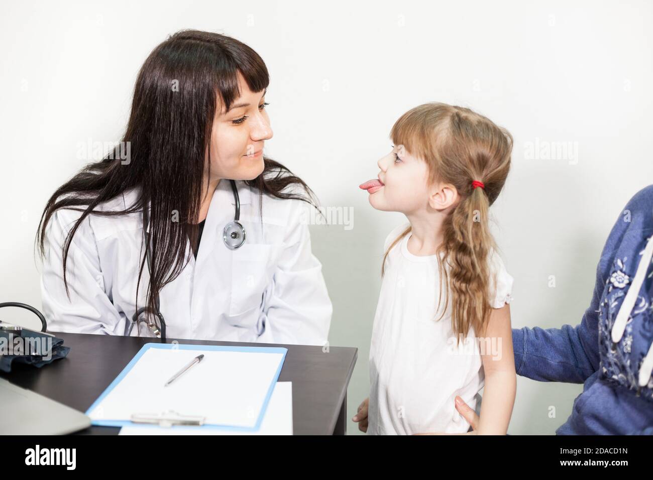 Portrait of little girl with opening mouth being examined by pediatrician doctor in medical office, kid with her mother Stock Photo