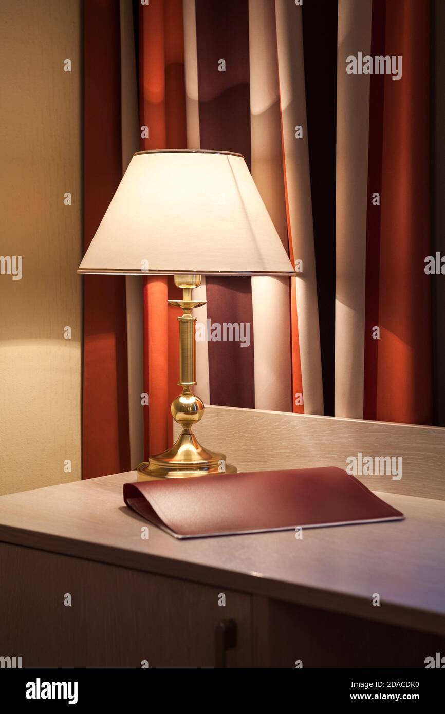 Reading lamp is on table in bedroom, closed window curtain, folder on desk Stock Photo