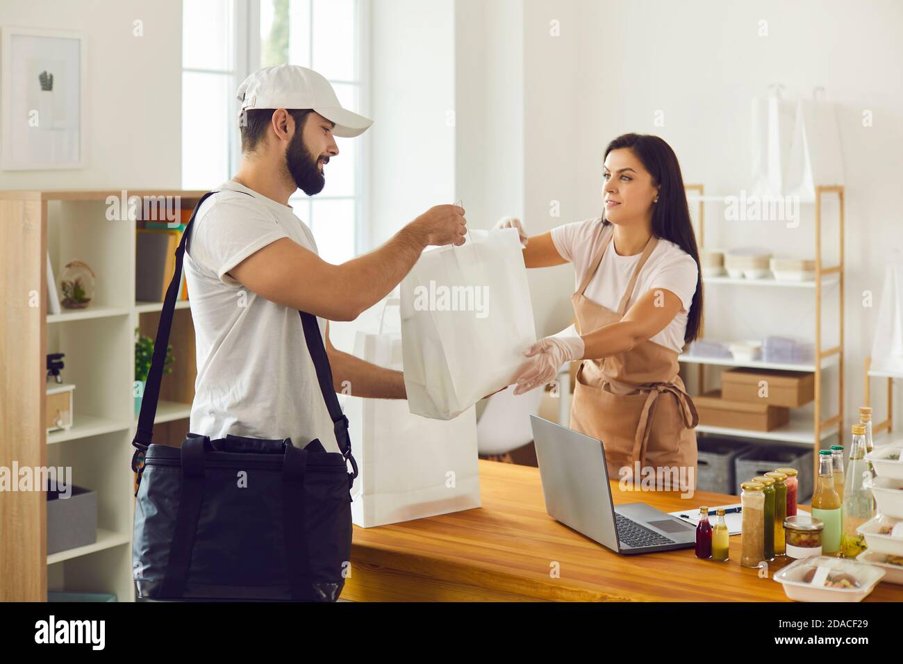 Young food delivery guy taking bags with packed lunch from takeaway cafe worker Stock Photo