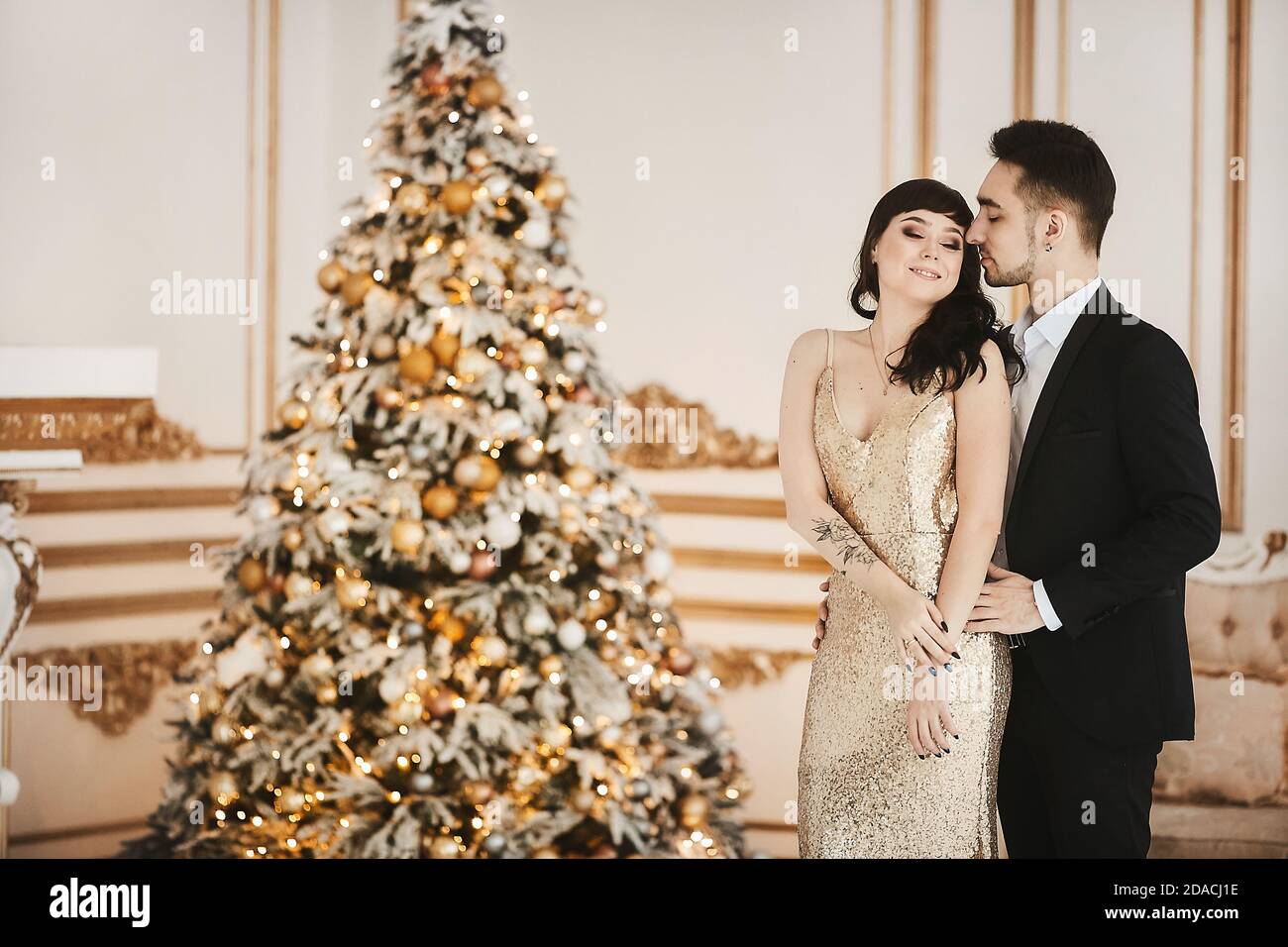 Model girl in an elegant gold dress and handsome gentleman in a black suit posing in a luxury interior near the Christmas tree Stock Photo Alamy