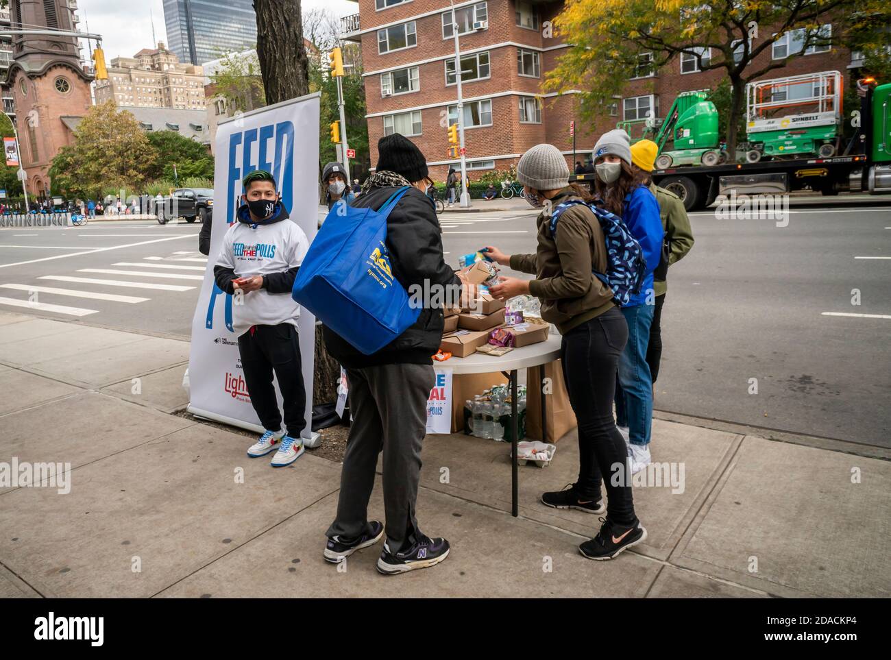 Volunteers from Feed the Polls distribute free lunch outside of the PS33 voting site in Chelsea in New York, while a member holds the sign down to prevent it from being blown away, on Election Day, Tuesday, November 3, 2020. (© Richard B. Levine) Stock Photo