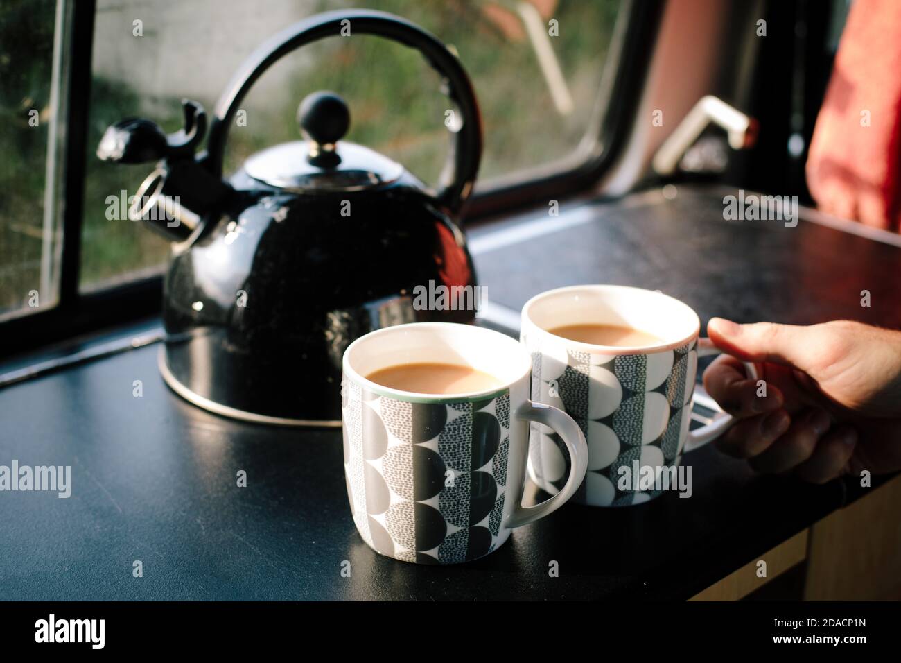 A whistling kettle and two cups of freshly made tea inside a campervan