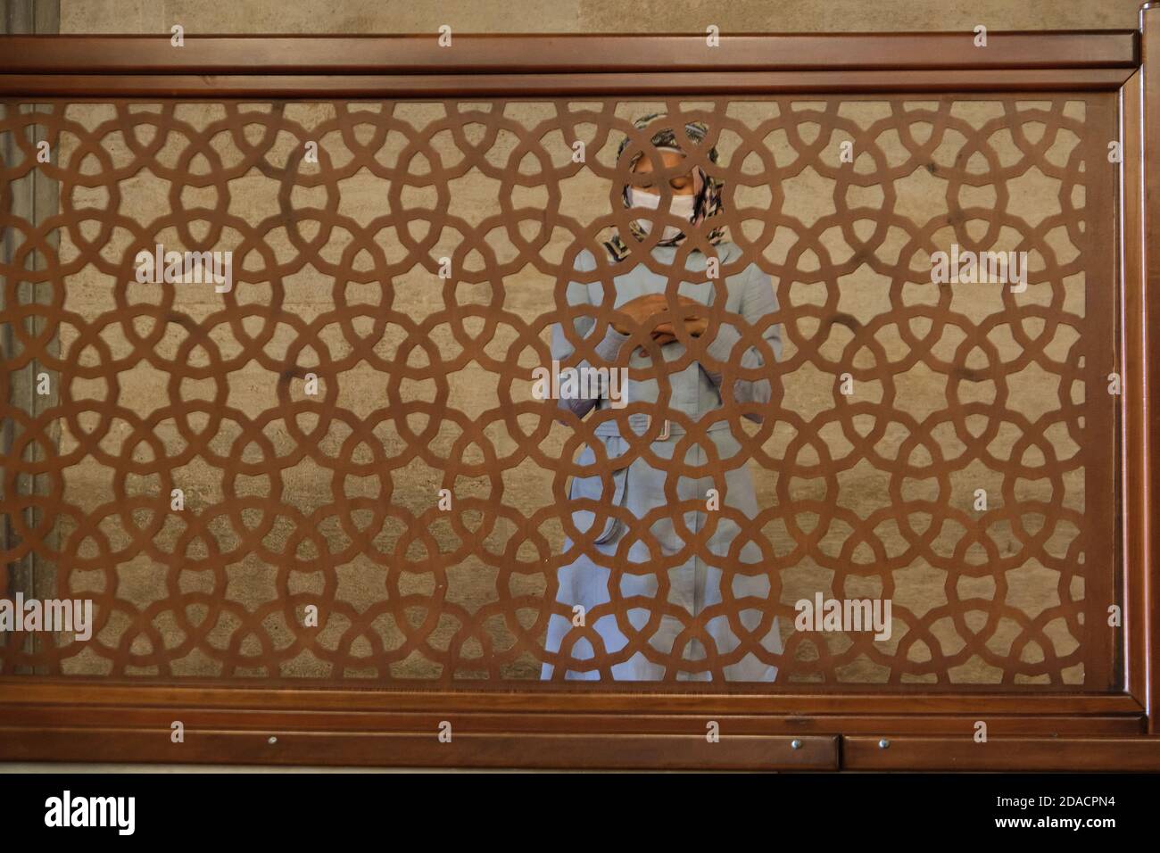 Muslim woman in hijab and wearing face mask praying with folded hands behind screen in mosque, Istanbul, Turkey Stock Photo