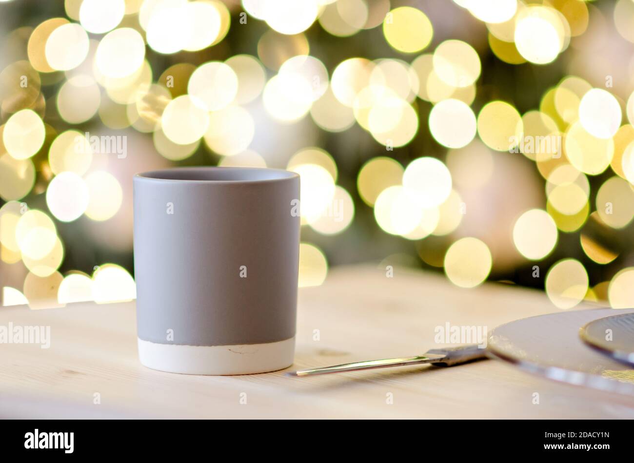 New year greeting card. On the wooden table is a gray cup of hot chocolate, decorated with a Christmas tree branch. Blurred bright yellow lights bokeh Stock Photo
