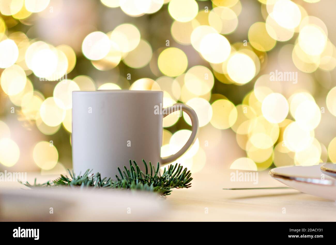 New year greeting card. On the wooden table is a gray cup of hot chocolate, decorated with a Christmas tree branch. Blurred bright yellow lights bokeh Stock Photo