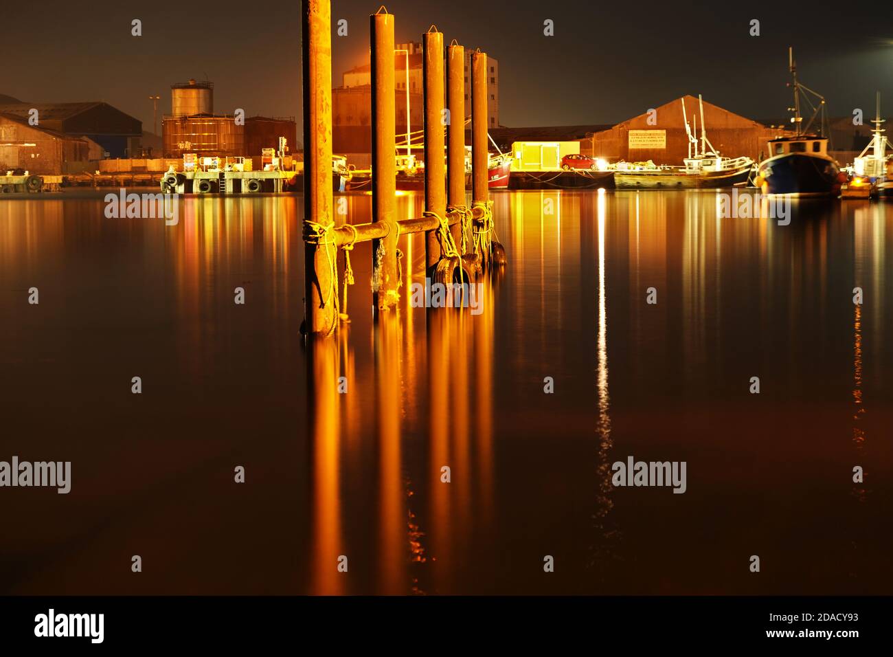 Tyres and rope hanging on metal post in Arklow harbour at night. Stock Photo