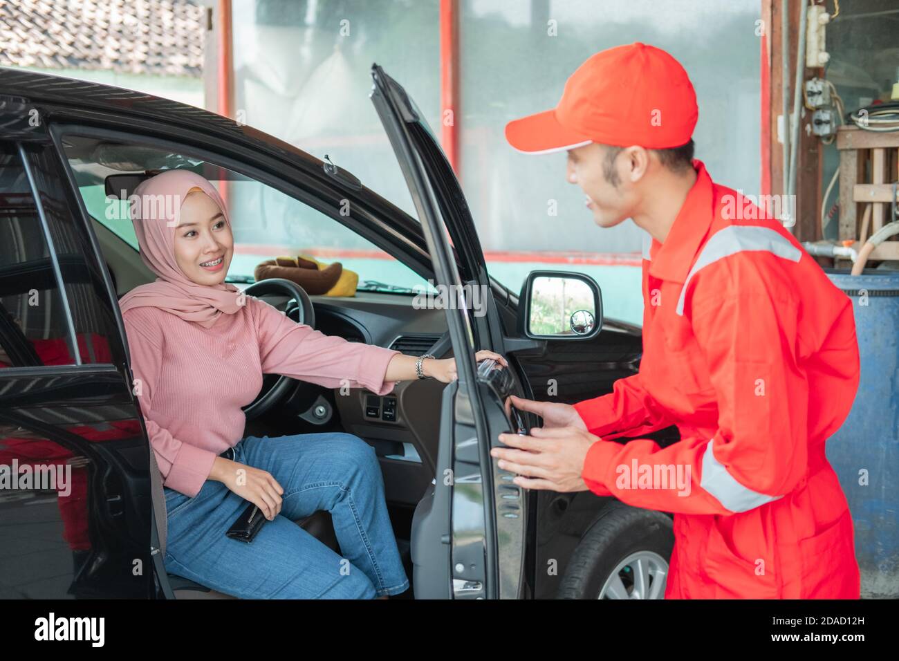 The mechanic in red uniform opens the car door when the customer comes