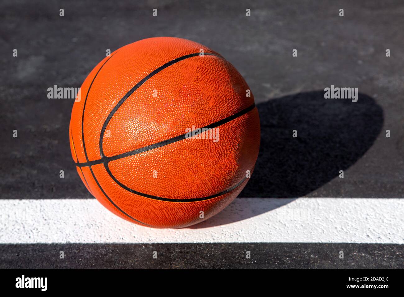 orange striped basketball ball stands on the white line marking the playing  field with asphalt tarmac, sports object lit by sun light on playground, n  Stock Photo - Alamy