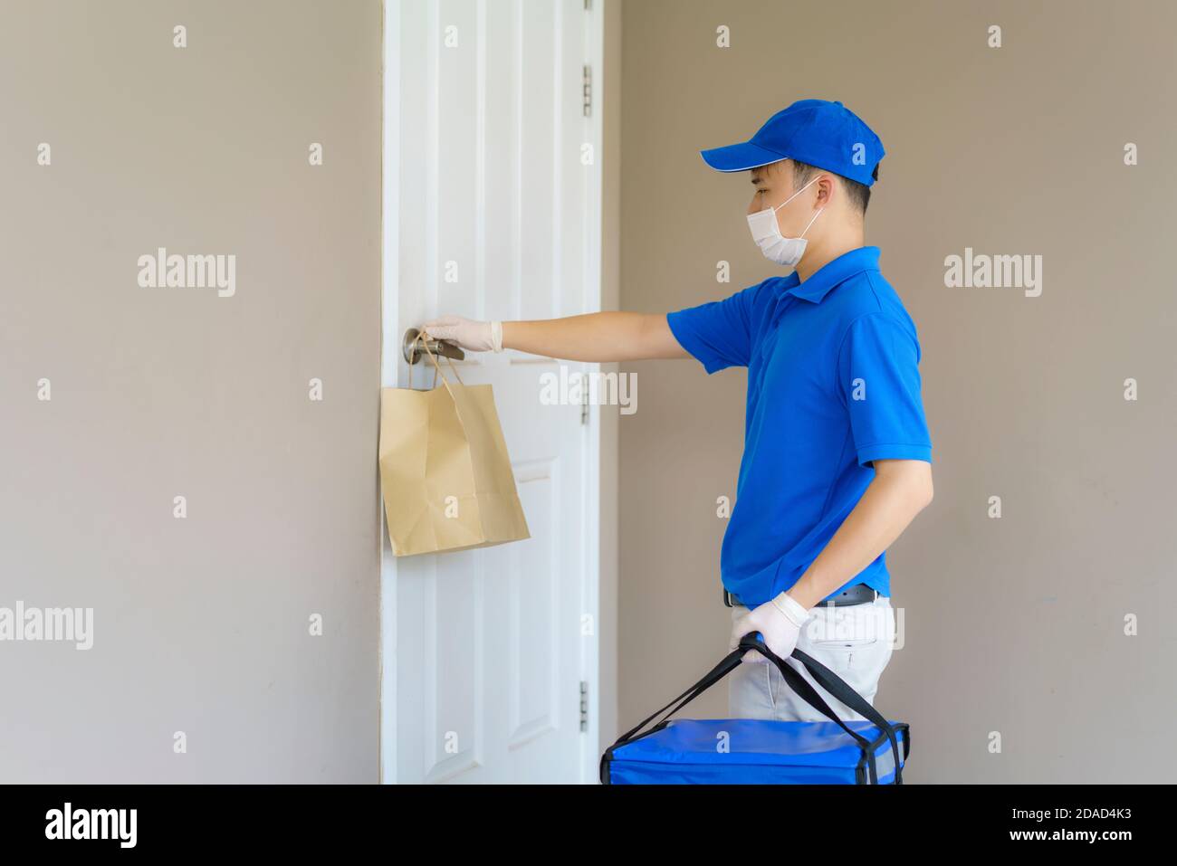 Asian delivery man send food bag at door knob for contactless or contact free from delivery rider in front house for social distancing for infection Stock Photo
