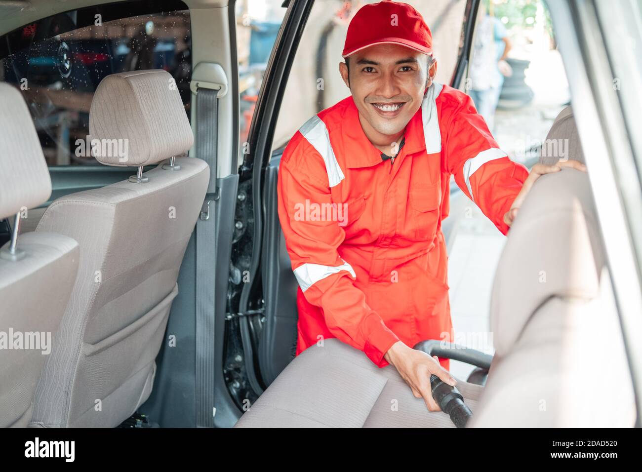 The male car cleaner wears a smiling red uniform while cleaning the