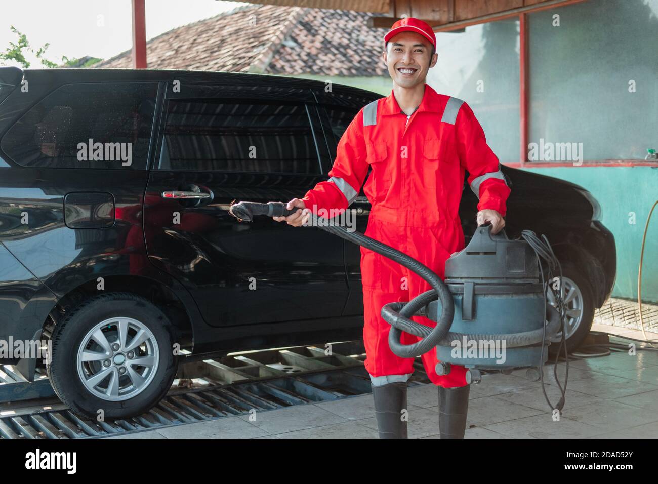 Male car cleaner wearing red uniform stands smiling while carrying