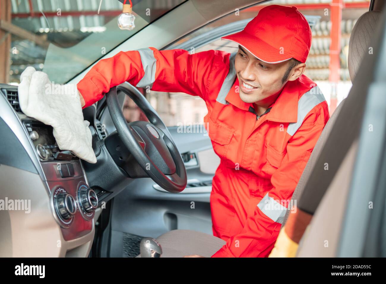 Male car cleaner wearing red uniform is wiping car interior dashboard