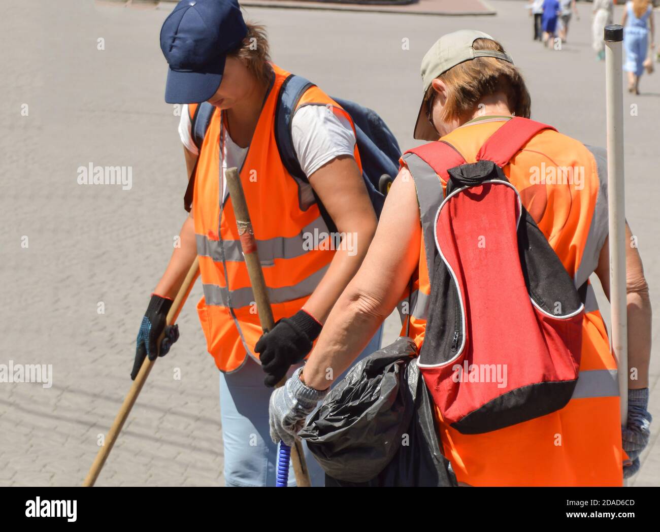 Two female cleaners in orange vests clean outside with tools, outdoor, summer Stock Photo