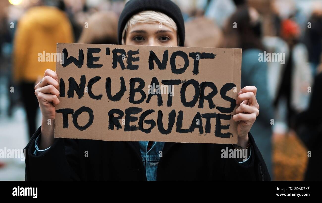Womens march. Young woman with face mask holding banner sign - We are not incubators to regulate. protest against strict abortion laws. High quality photo Stock Photo