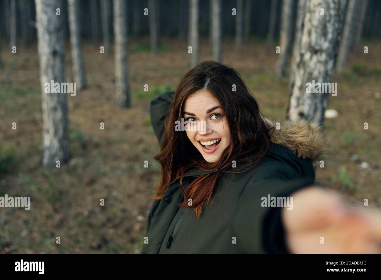 Cheerful woman in warm jacket in nature with outstretched hand on the background of the autumn forest Stock Photo