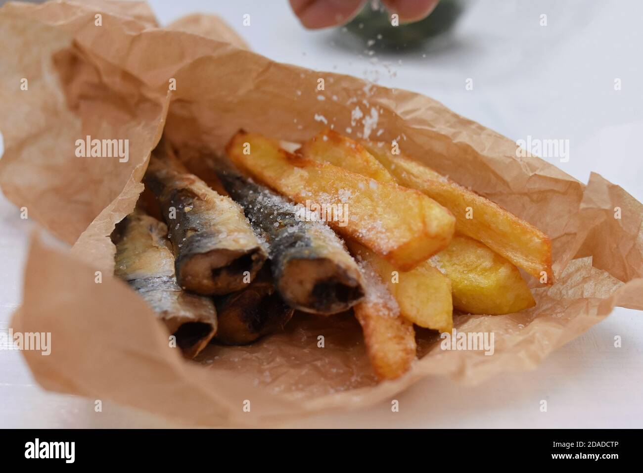Spreading salt over Fish and chips in a paper wrapper/ Yummy takeaway food Stock Photo