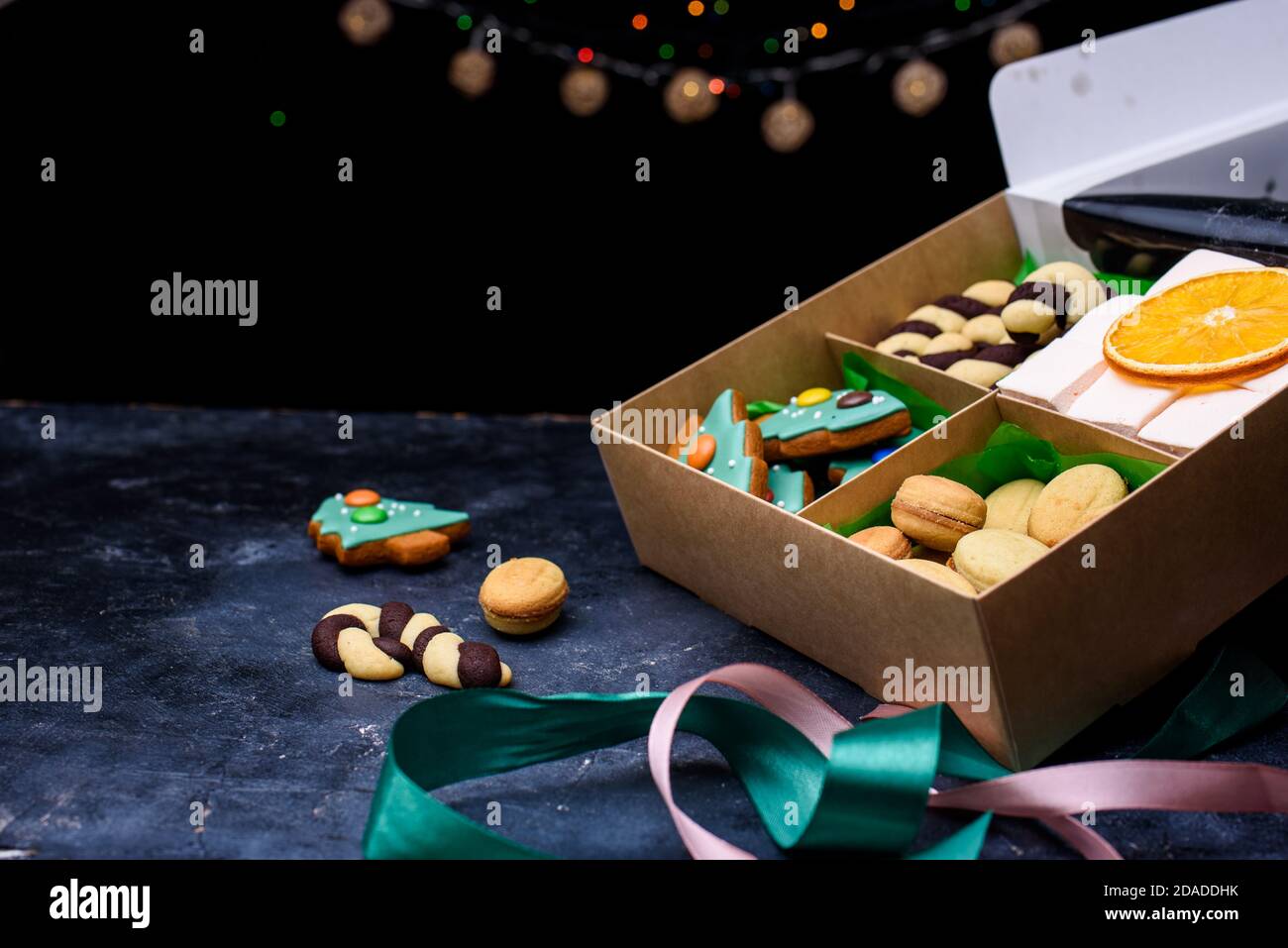 Box with satin ribbons and delicious treats for New Year and Christmas. New Year's desserts on a dark background. New Year's content Stock Photo