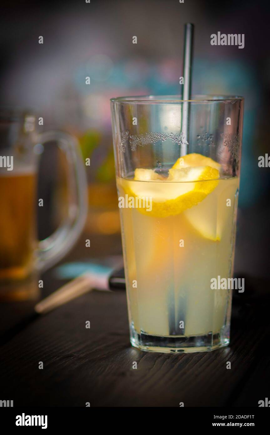 bright lucent yellow drink (lemonade) with lemon slices and in dark closeup, on a wood table, non-alcoholic drink Stock Photo