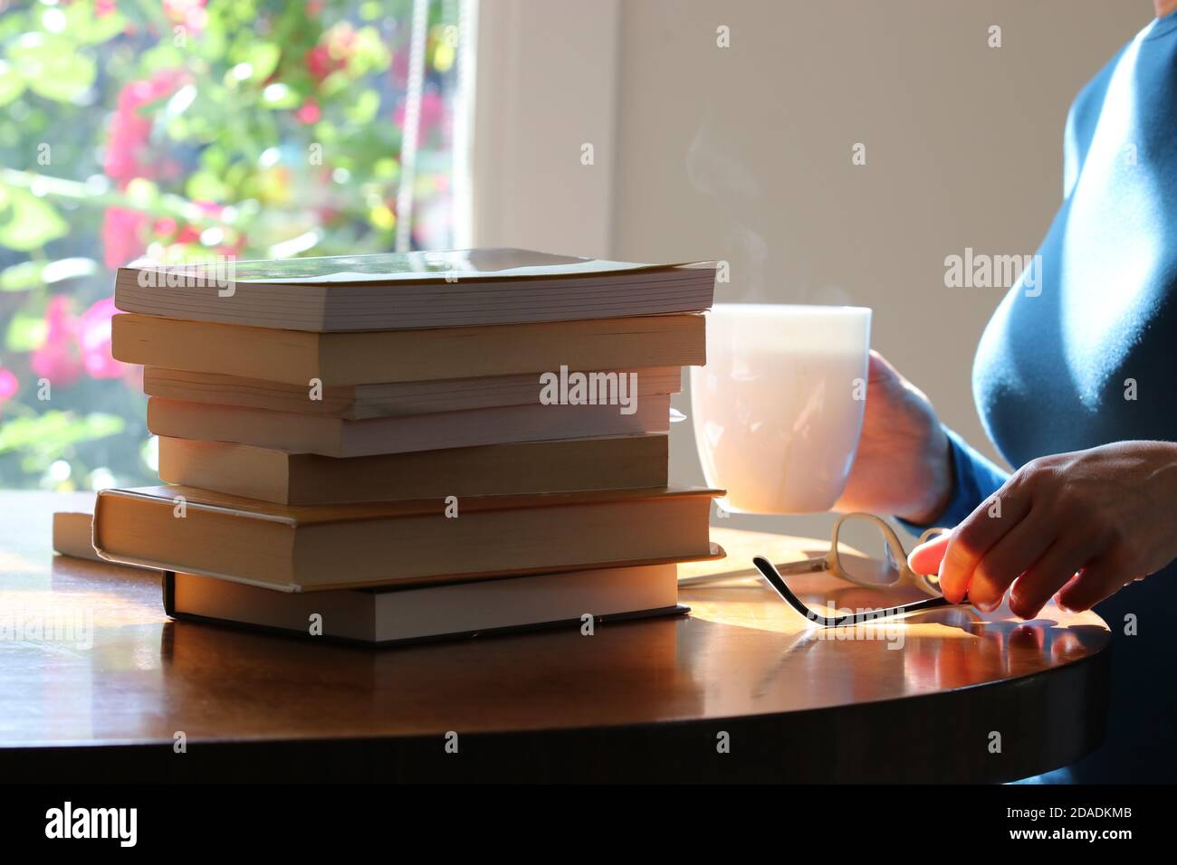 Woman with eye glasses sitting at table with a pile of books Stock Photo