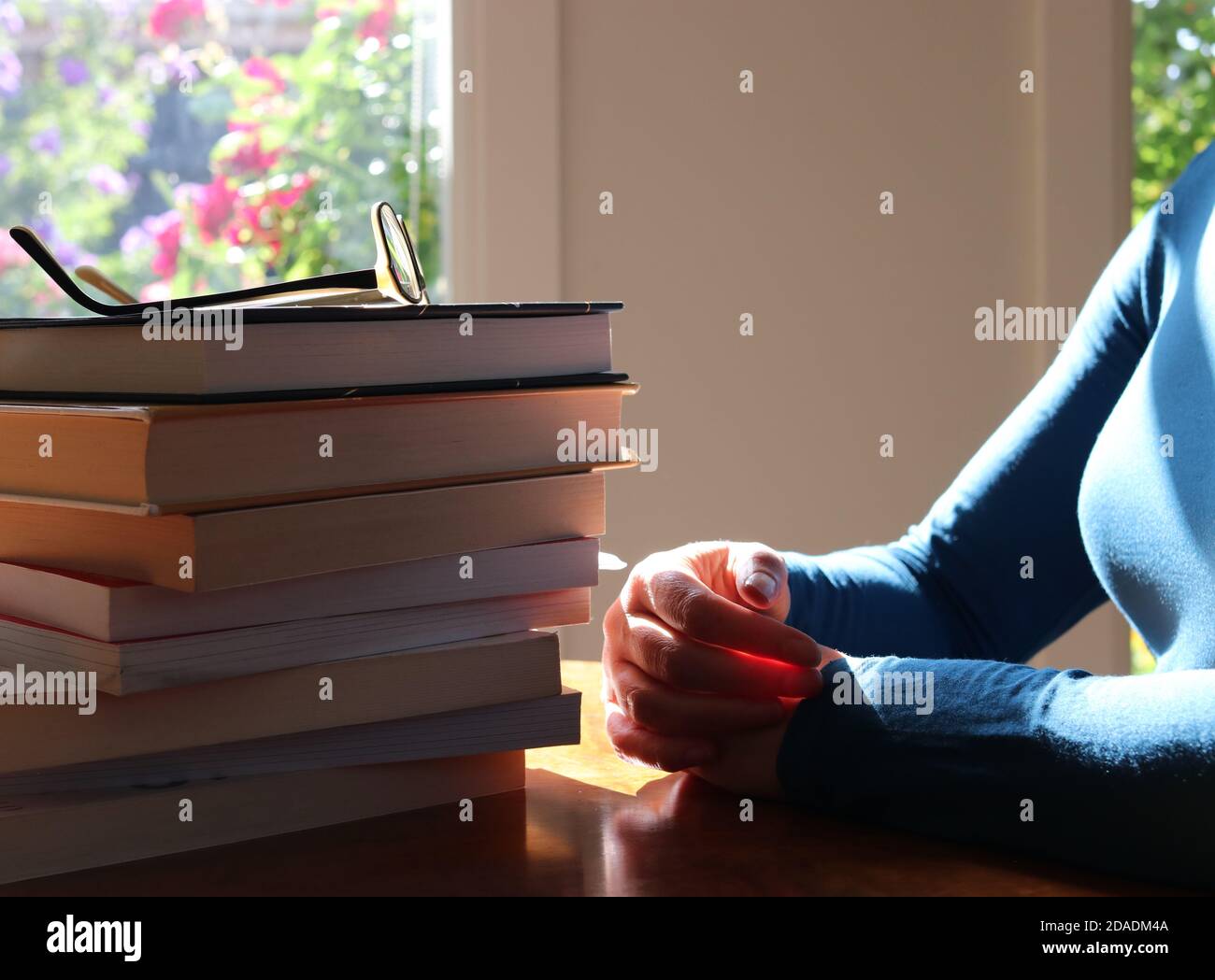 Woman with eye glasses sitting at table with a pile of books Stock Photo