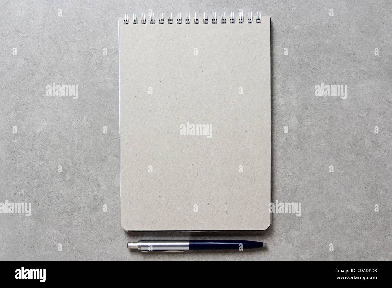 A spring notebook with a sheet of craft paper A5 with a ballpoint pen on light grey concrete background. Concept of new idea, business plan and strategy, development and implementation of content. Empty space for text. Stock Photo