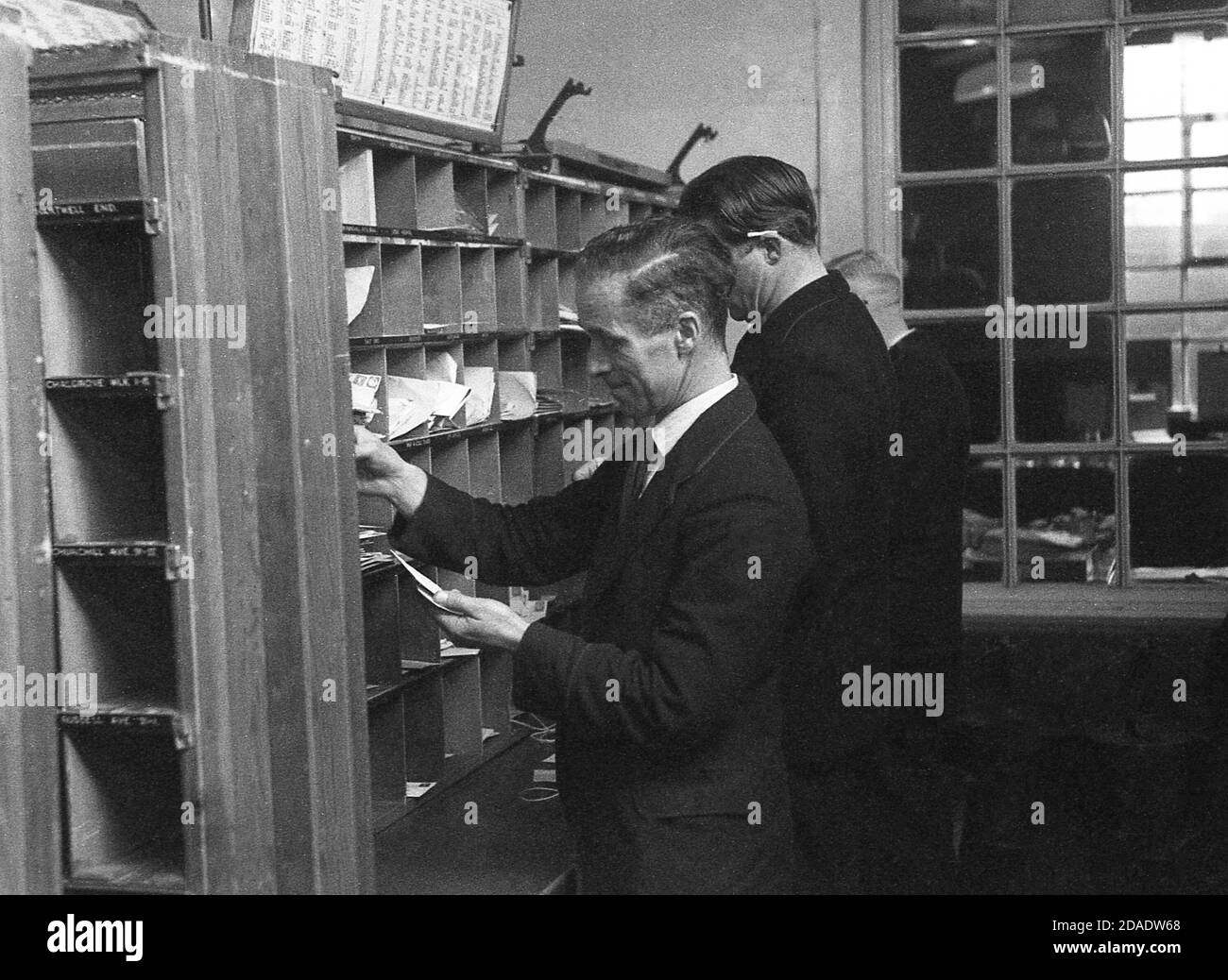 1950s, historical picture of GPO employees putting letters or mail into the individual cuppy holes on a sideboard, London, England, UK. As can be seen, in this era there was no mechanisation and all letters had to be sorted by hand and on a wall unit, the letters would be put into the correct little section or cubby hole based on areas or districts. Stock Photo