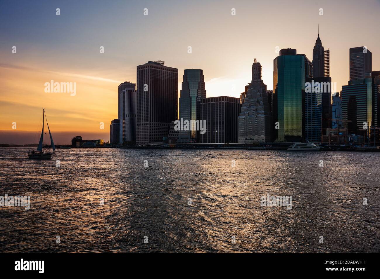 Sailing boat in the waters of the East River at sunset and Manhattan ...