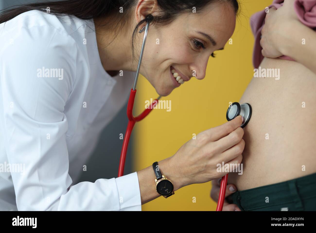 Doctor listens with stethoscope to the belly of pregnant woman Stock