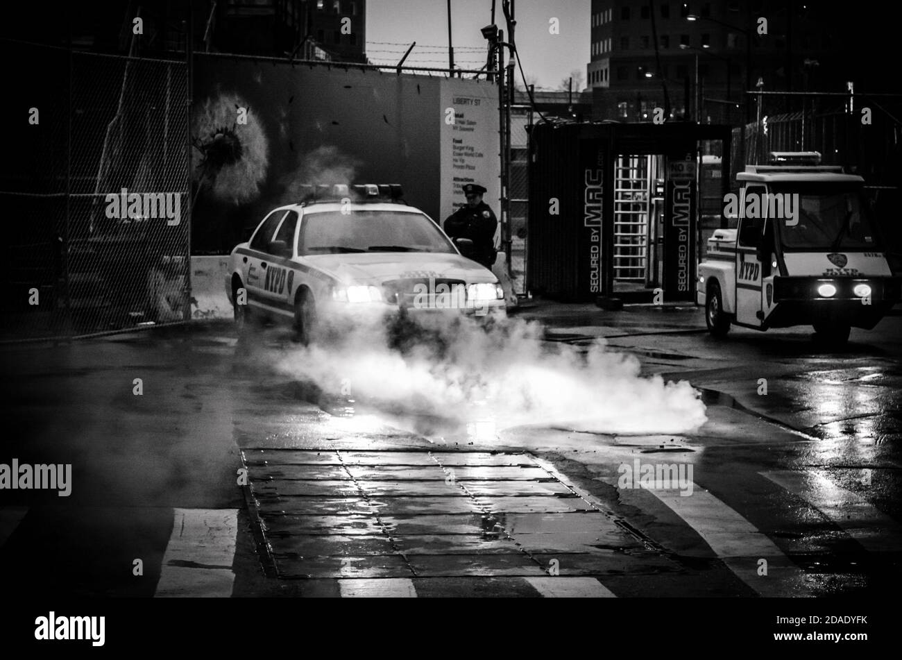 Black and White Photo of a Police Vehicle with its Headlights Shed Light on Steam Cominf of the Sewers in Lower Manhattan, New York City, USA Stock Photo