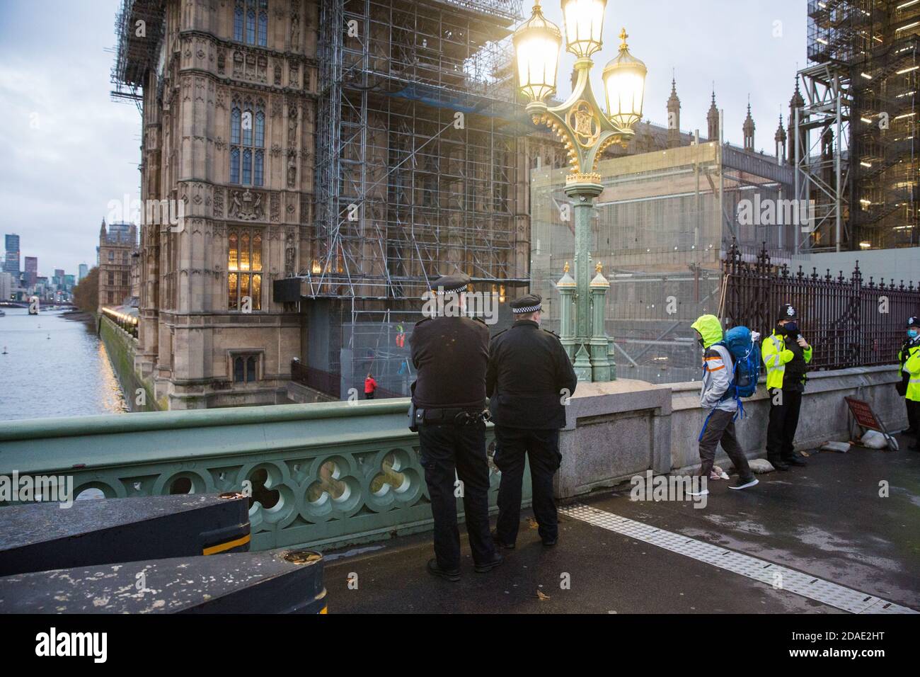 London, UK. 12th November, 2020. Police officers observe activists from the group Action for Climate Truth and Reparations (ACTR) climbing scaffolding at dawn to hang an open letter to the UK people from Africans Rising For Justice, Peace and Dignity from the Houses of Parliament. The letter, which launches Africans Rising’s ReRight History campaign, contains a plea to the UK people to start making amends for the harm caused by slavery and colonialism.  Credit: Mark Kerrison/Alamy Live News Stock Photo