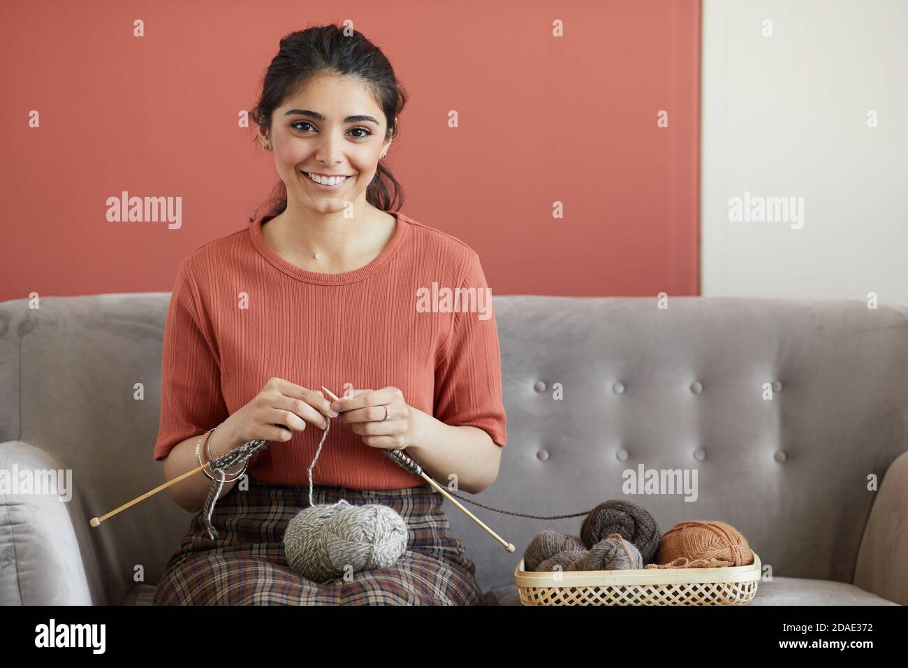 Portrait of happy housewife smiling at camera while sitting on sofa in ...