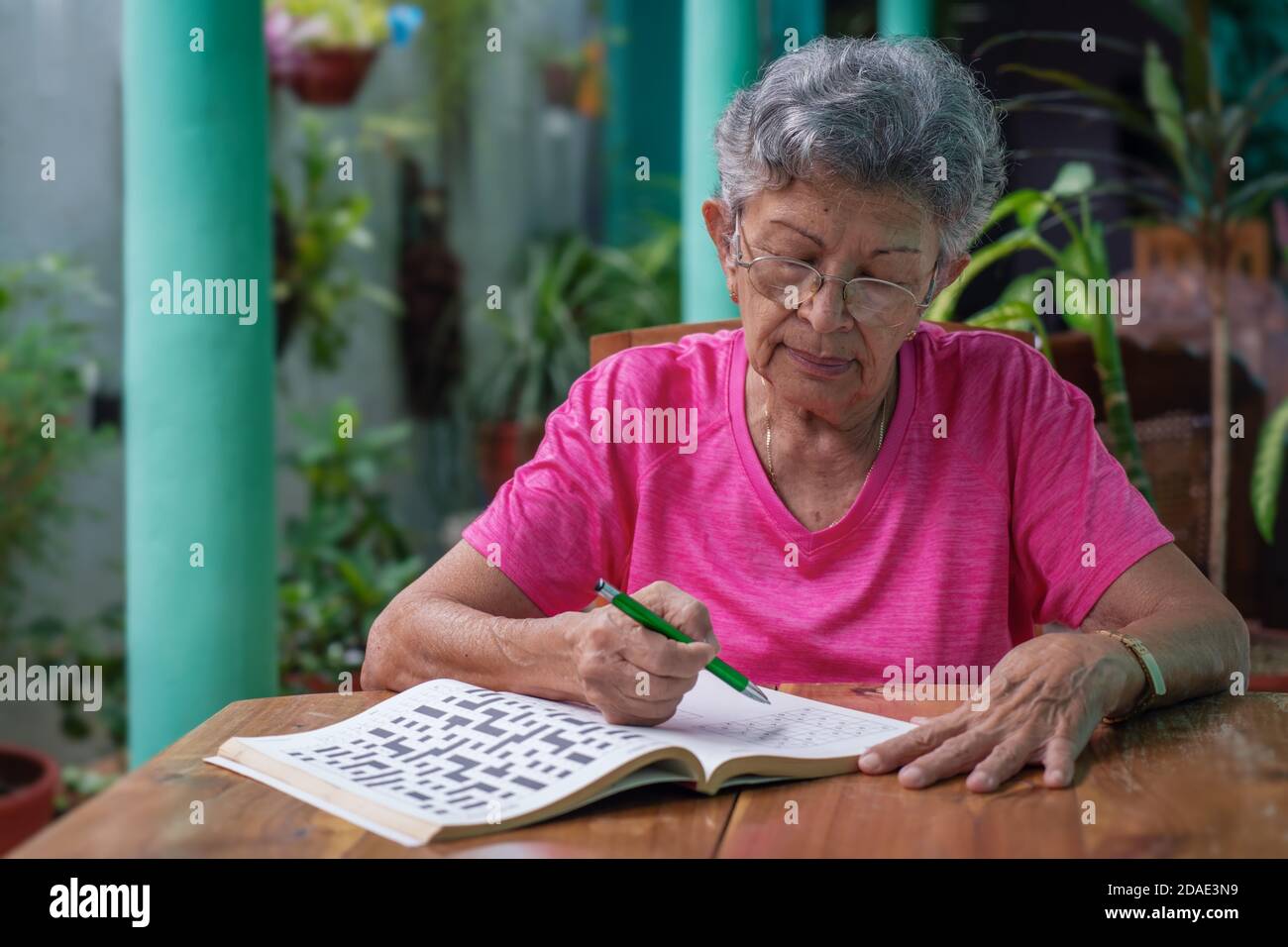 Senior woman with glasses sitting at a table, filling in a sudoku puzzle Stock Photo