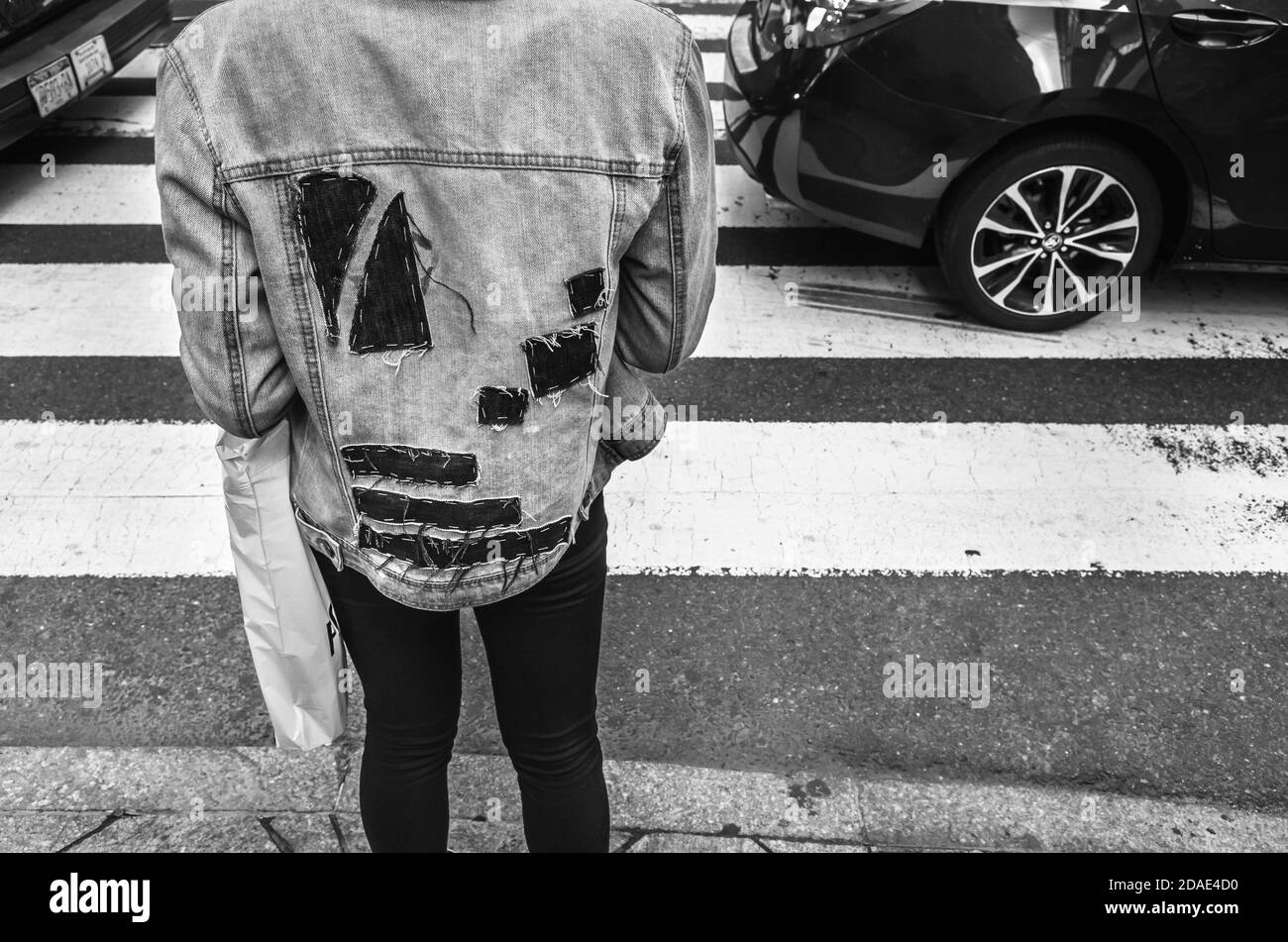 New York, USA - Sep 24, 2018:  Black and white image of Manhattan street scene. Man’s back view in a denim jacket with large black patches at a pedest Stock Photo