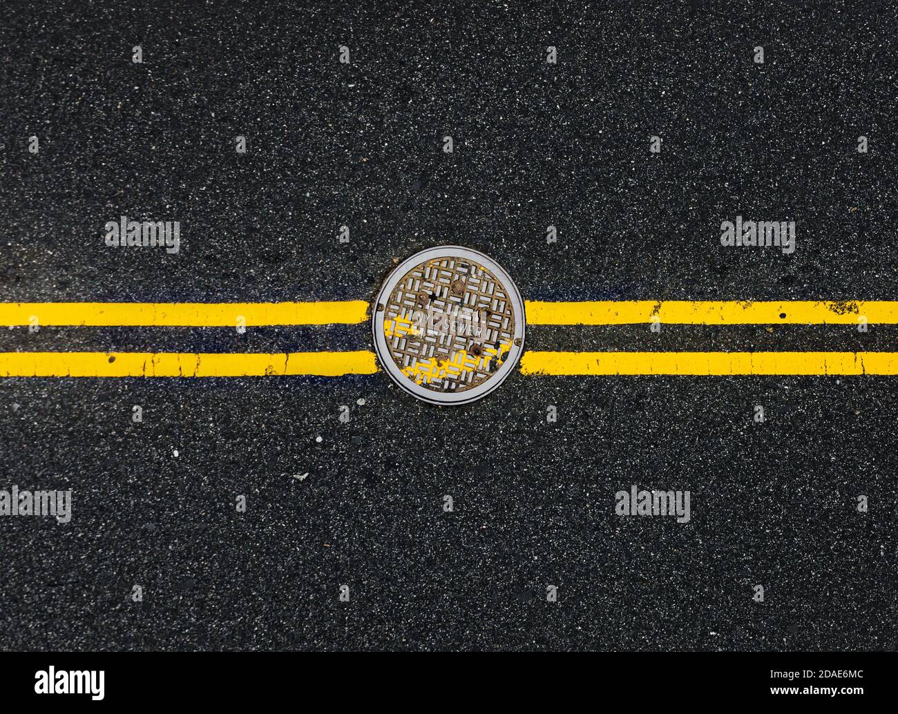 Yellow double solid line with the hatch cover. Road markings on asphalt on the street of Manhattan in New York City. Words NYC sewer on the hatch cove Stock Photo