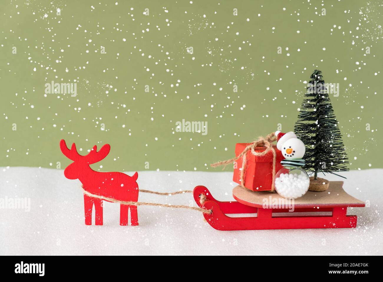 Toy reindeer and sleigh delivering Christmas present and tree on green background. Stock Photo