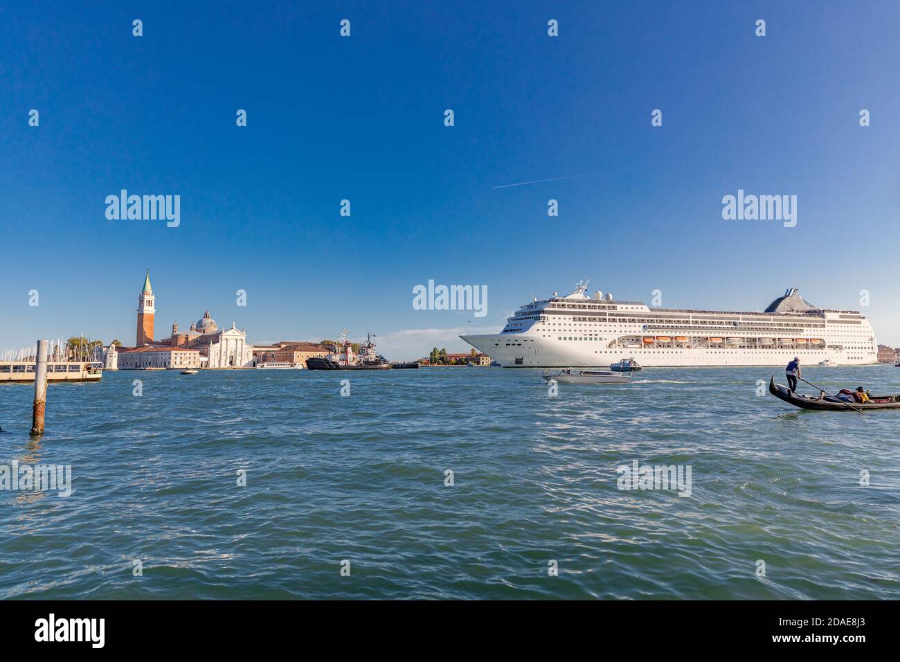 Venice, Italy - 09.11.19: Gondola & huge cruise ship in Giudecca Canal. Many people affirm that the environmental impact of big cruise ships Stock Photo