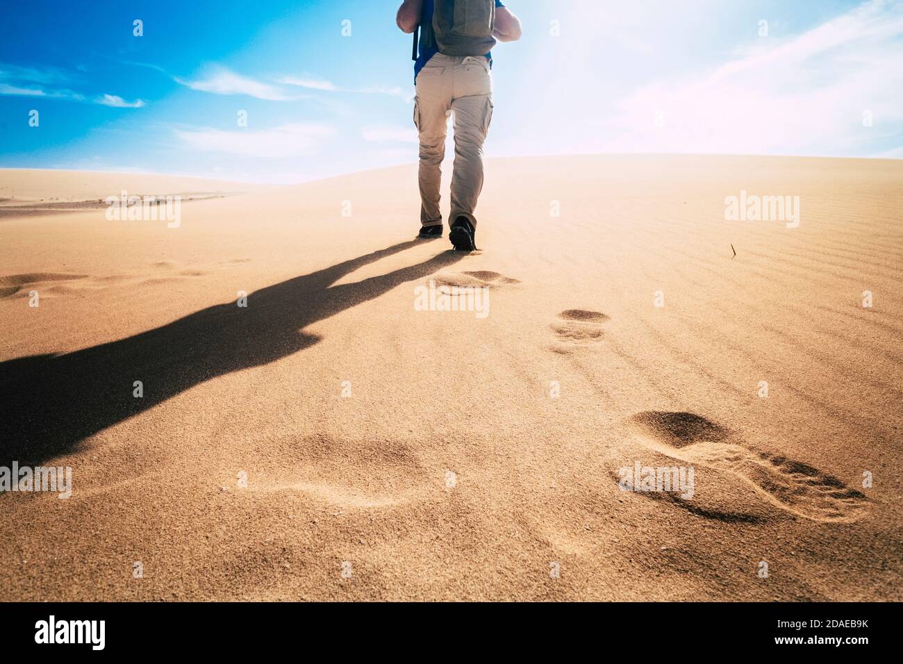 Adventure and explore in a changed planet earth for climate warming concept - man viewed from back walking on a desert dunes with blue sky in background Stock Photo