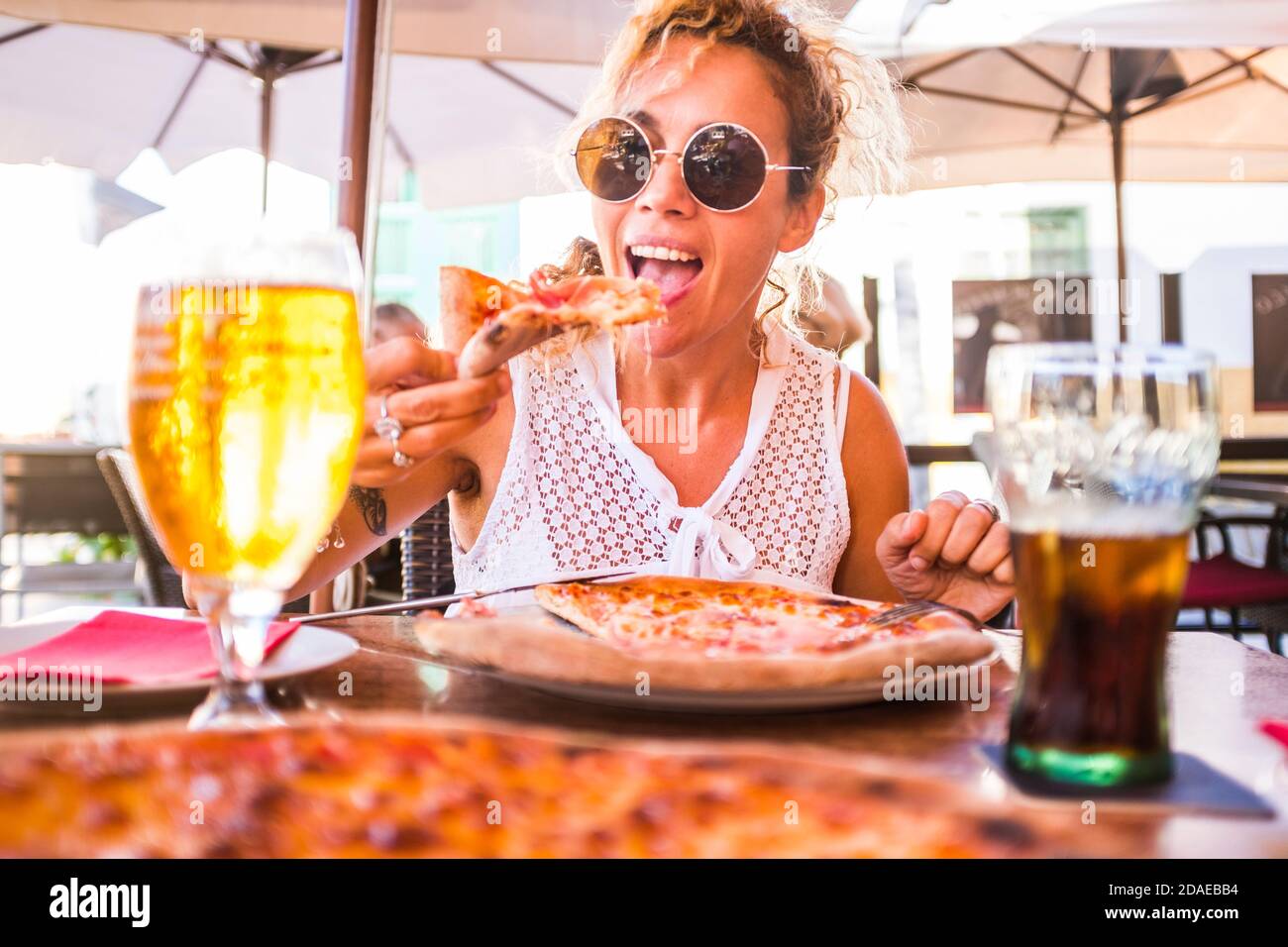Happy young adult caucasian woman eating a beautiful and tasty healthy pizza at the restaurant - concept of happy people and food relationship - italian style life and summer leisure vacation activity Stock Photo