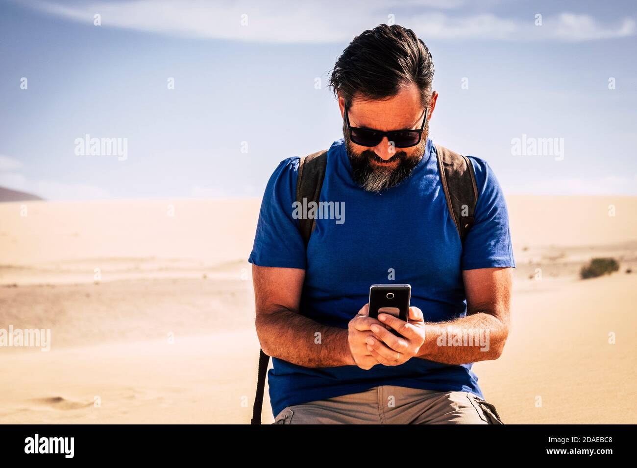 Adult caucasian man use internet connection with modern phone in the middle of the desert dunes sand - people travel and adventure concept - warm planet and climate change danger Stock Photo