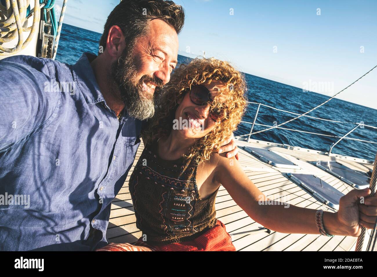 Happy adult caucasian couple together on a sailboat enjoy vacation or excursion - people in outdoor leisure activity on boat with blue ocean and sky around . happiness and love man and woman Stock Photo