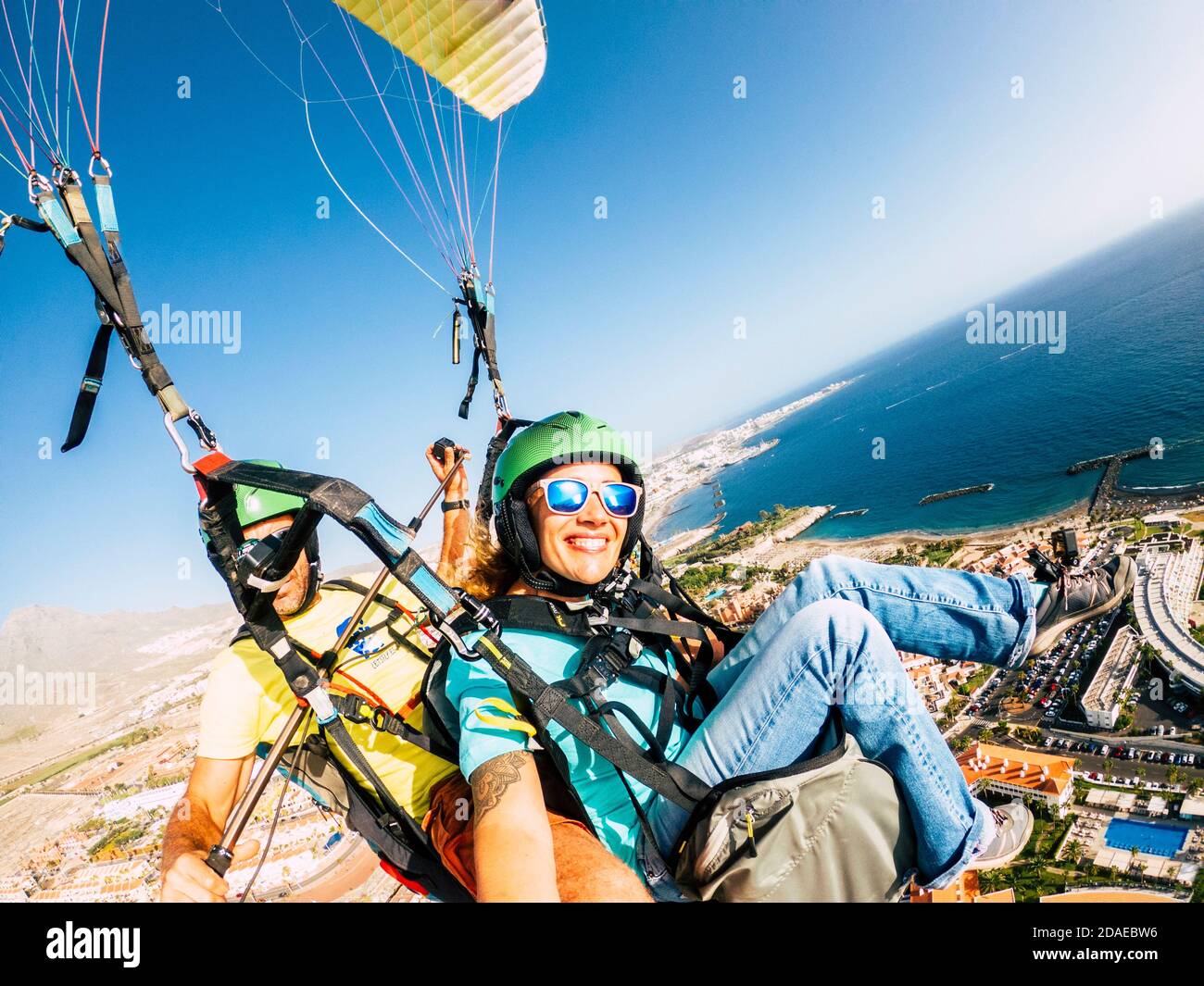 Cheerful happy woman to paraglyde experience with pilot - couple having fun in the air paraglyding over the city with coastline view - tourist and summer holiday vacation active people Stock Photo
