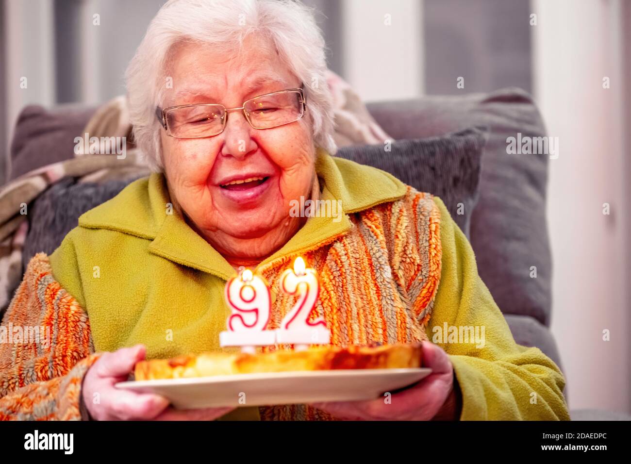 Old woman with birthday cake blowing out candles sitting in armchair