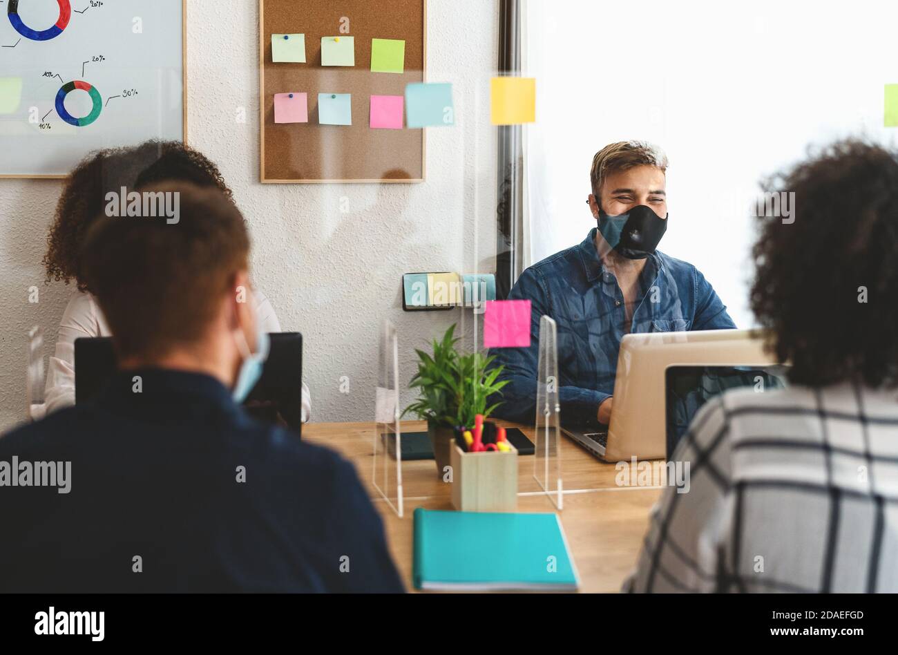 Young people in co-working creative space wearing surgical mask and keeping social distance to avoid corona virus spread Stock Photo