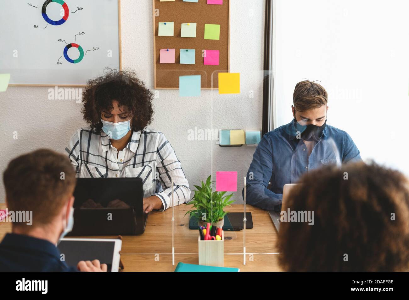 Young people in co-working creative space wearing surgical mask and keeping social distance to avoid corona virus spread Stock Photo